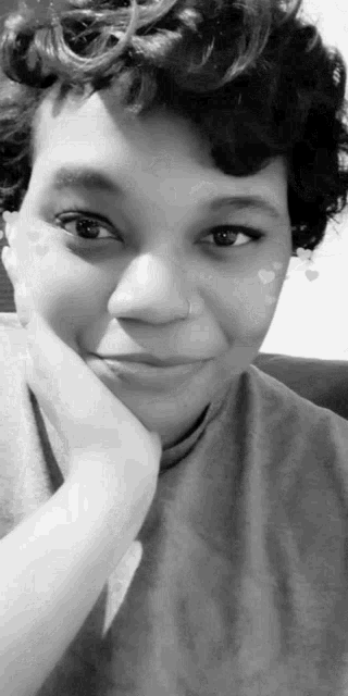 a black and white photo of a woman smiling with her hand on her chin .
