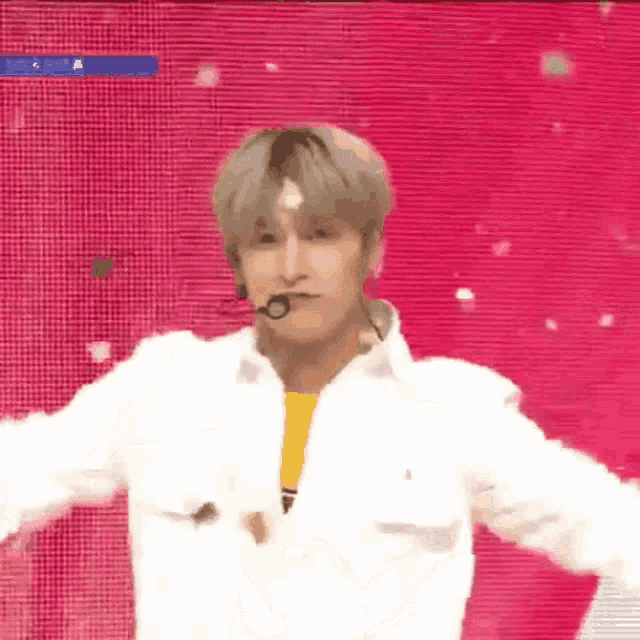 a man wearing a white jacket and a yellow shirt is dancing on a stage with a pink background .