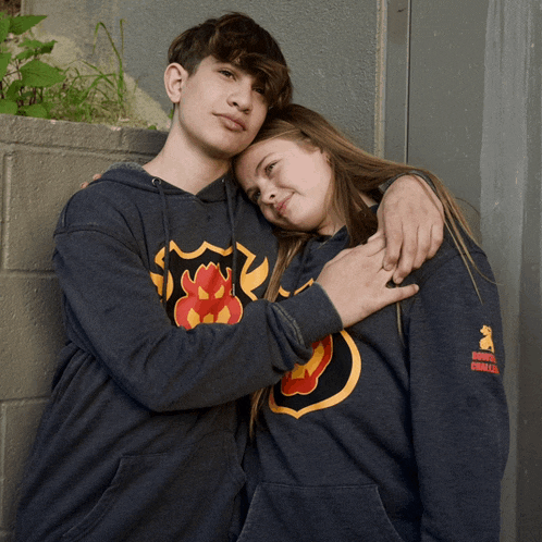 a boy and a girl are posing for a picture and the girl is wearing a sweatshirt with a dragon on the back