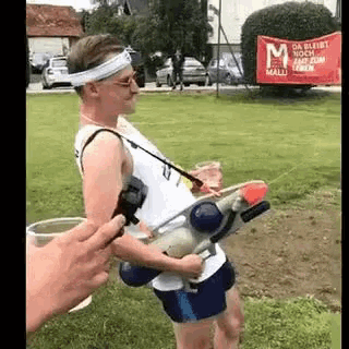 a man is holding a water gun in his hand while standing in a field .