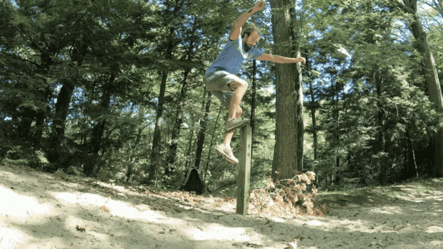 a man in a blue shirt is jumping over a wooden post