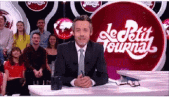 a man in a suit and tie is sitting at a table in front of a sign that says le petit journal