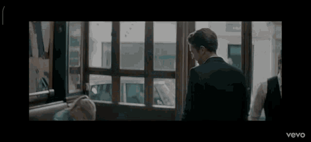 a man in a suit stands in front of a window in a dark room .