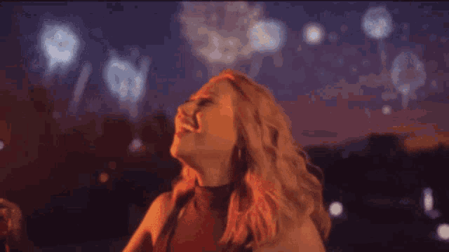a woman in a red top is looking up at fireworks in the sky .