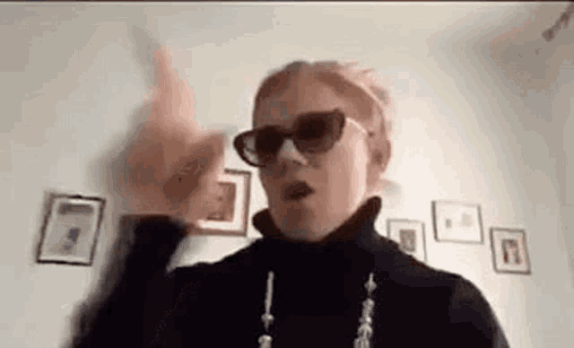 a woman wearing sunglasses and a turtleneck is making a funny face .