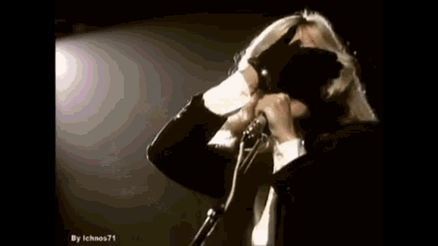 a woman in a black suit and tie is singing into a microphone .