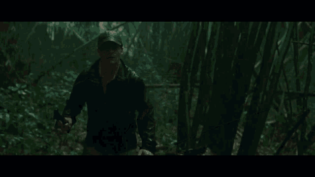 a man in a hat is walking through a dark forest holding a gun