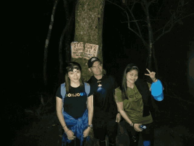 three people standing in front of a tree with a sign that says station campsite 1
