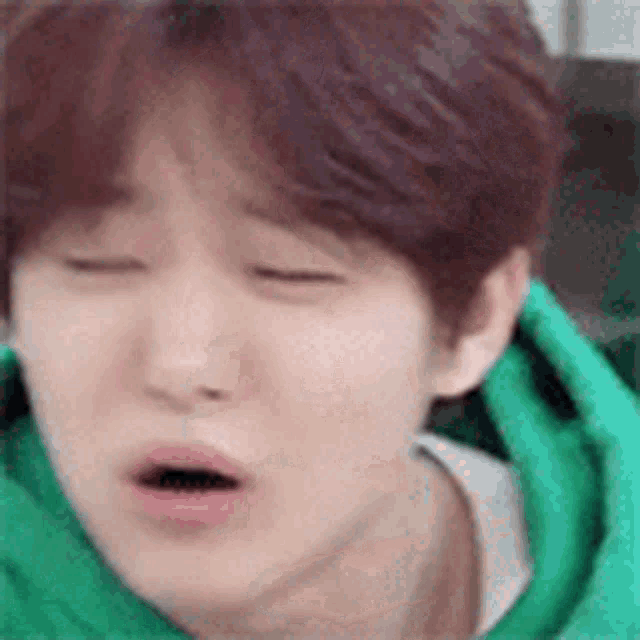 a close up of a person 's face with their eyes closed and a green hoodie on .