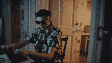 a man wearing sunglasses and a hawaiian shirt is typing on a laptop