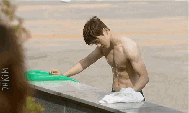 a shirtless man is leaning against a wall with the word kim on the bottom right
