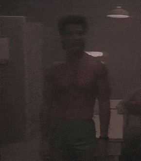 a shirtless man stands in a dark room
