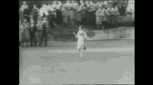 a black and white photo of a person running on a field with a crowd watching .