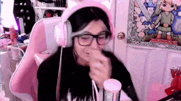 a girl wearing headphones and glasses is sitting in a pink chair and making a funny face .