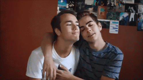 two young men are hugging each other in front of a wall covered in pictures .