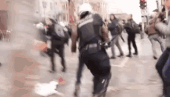 a blurry picture of a police officer fighting a crowd of protesters .