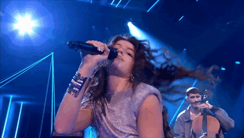 a woman singing into a microphone with a man playing a violin behind her
