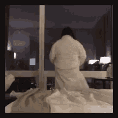 a person in a white robe is standing on a bed in front of a window