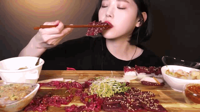 a woman is eating meat with chopsticks while wearing ear buds