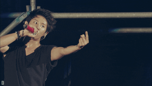 a man in a black shirt is singing into a microphone and giving the middle finger
