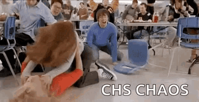 a group of people are fighting in a school cafeteria with chairs on the floor .