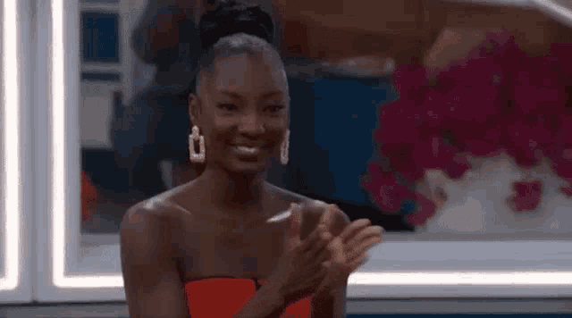 a woman in a red dress and earrings is clapping her hands .