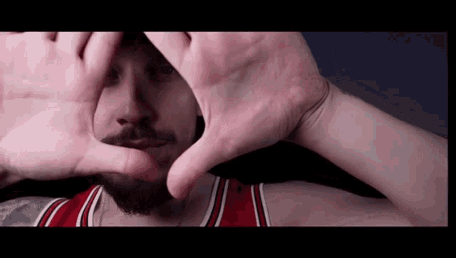 a man making a frame with his hands while wearing a red and white jersey