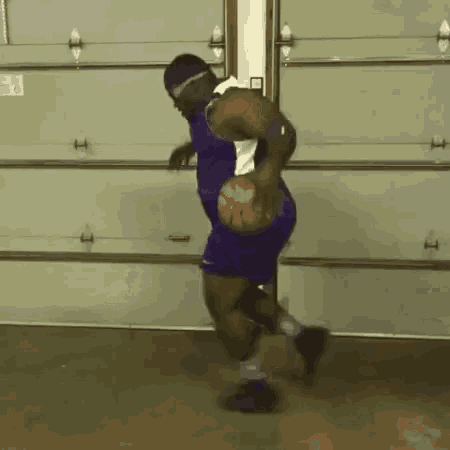 a man in a purple jersey is playing basketball in a garage .