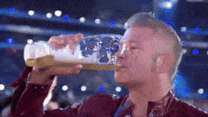 a man is drinking beer from a bottle with the number 12 on it .