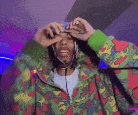a man wearing headphones and a colorful jacket is holding a cigarette to his face