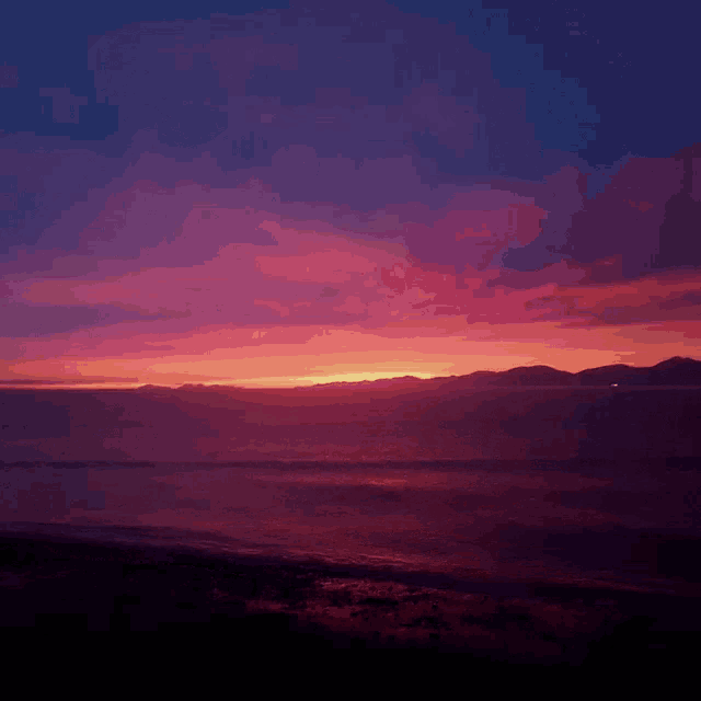 sunset over the ocean with mountains in the background