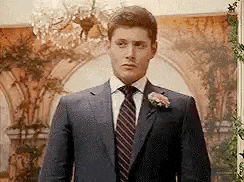 a man in a suit and tie is standing in a room with a chandelier .
