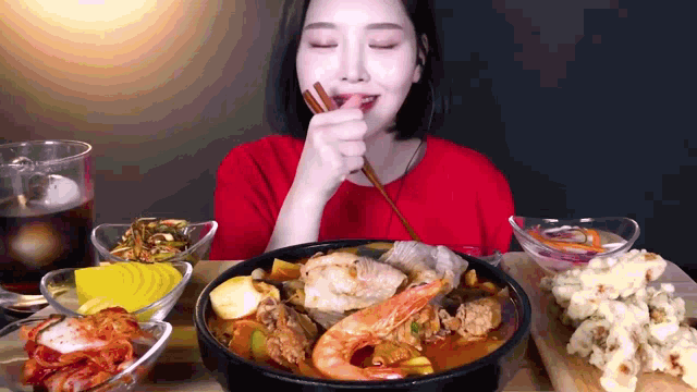 a woman in a red shirt is eating a meal with chopsticks .