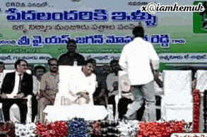 a man stands on a stage in front of a crowd with a sign above him that says ' x @iamhemuh '