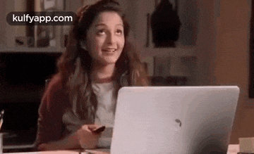 a woman is sitting at a table with a laptop computer and a cell phone .