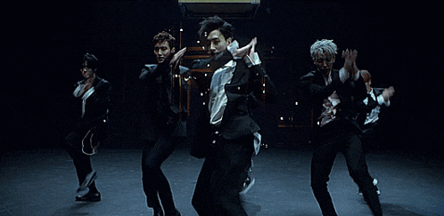 a group of young men in suits are dancing on a stage