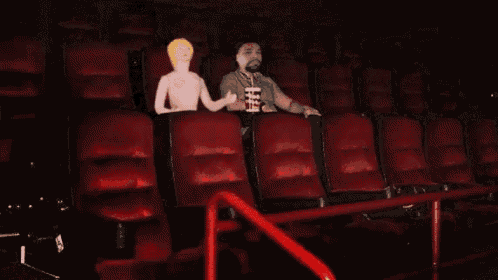 a man sits in a movie theater holding a cup of popcorn