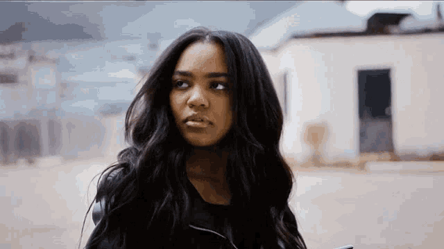 a woman with long black hair is standing in front of a building looking at the camera .