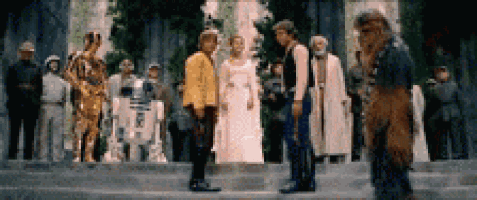 a group of people standing in front of a building with a r2d2 robot in the background