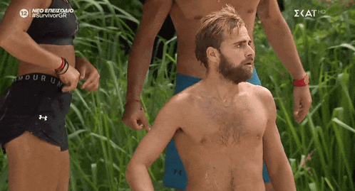 a man without a shirt is standing in a field with a woman wearing under armour shorts behind him
