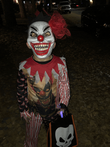 a child dressed in a clown costume holds a trick or treat bag with a skull on it