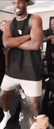 a man in a tank top and shorts is standing with his arms crossed in a gym .