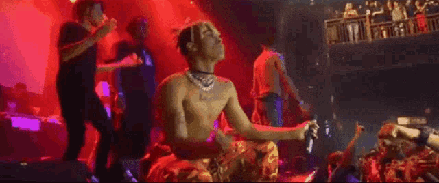 a man without a shirt is sitting on a stage in front of a crowd of people .