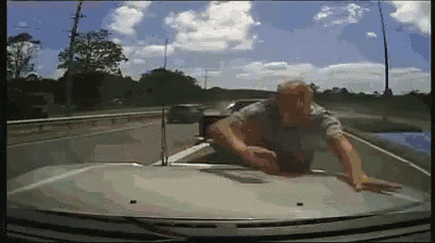 a man is crawling on the hood of a car on a highway .