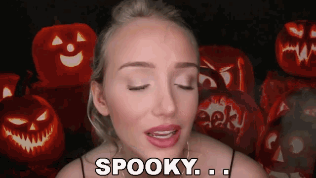 a woman says spooky in front of a pile of carved pumpkins