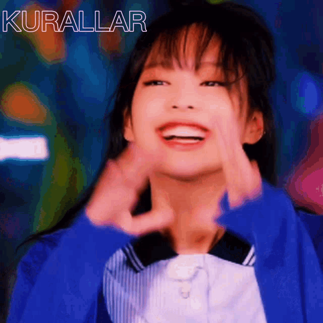 a girl in a blue jacket is smiling and making a heart with her hands