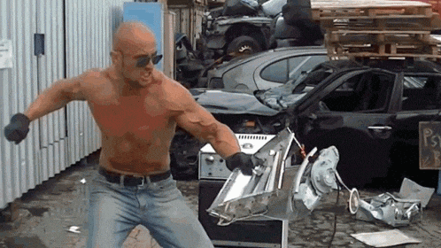 a man without a shirt is standing in front of a pile of junk