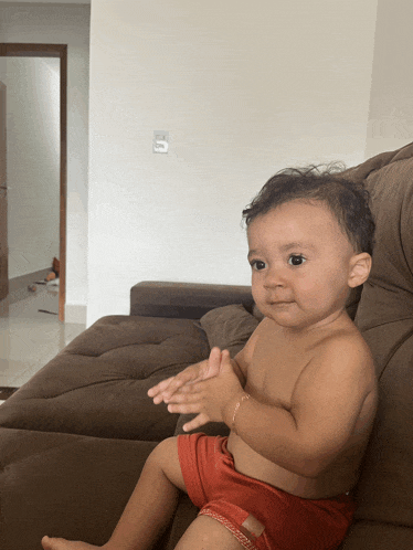 a baby is sitting on a couch and clapping