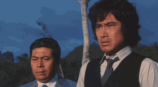 a man in a suit and tie stands next to another man in a vest
