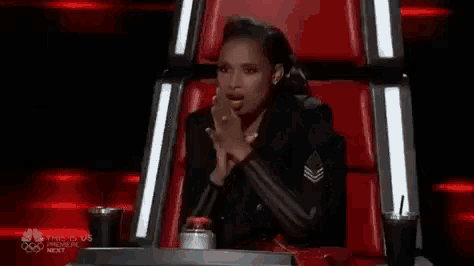 a woman is sitting in a red chair with her hands folded and drinking a soda .